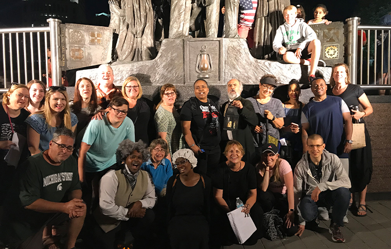 Large group of people posing in front of a monument to the Underground Railroad on a Detroit Underground Railroad Walking Tour